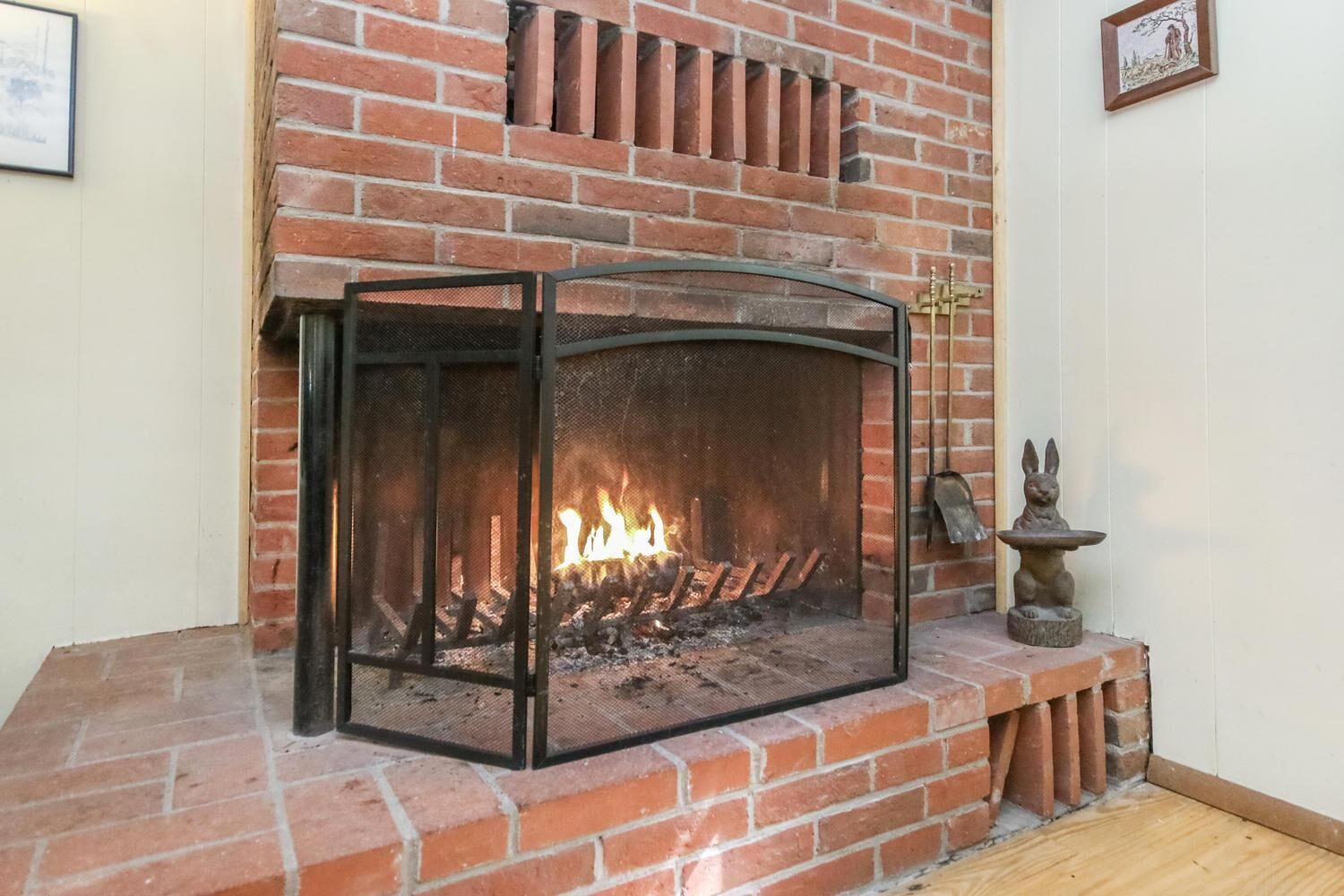 A fireplace with a glass screen, a brick wall, and a small statue of a rabbit on a stand.