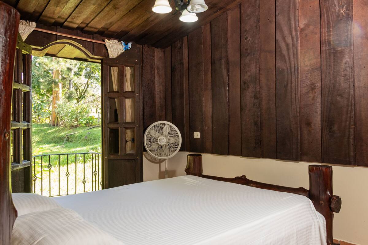 A wooden room with a bed, a fan, and a door leading to a balcony.