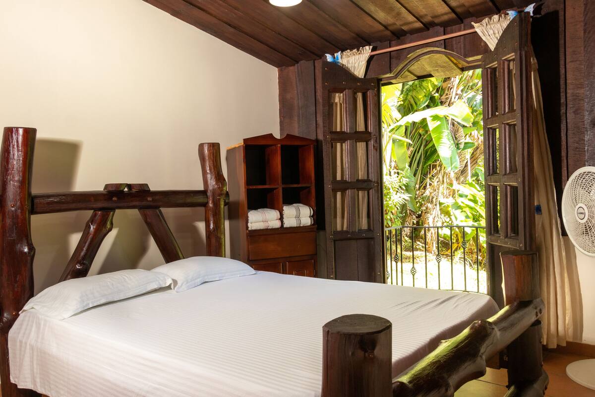 A wooden bed with a white mattress, a wooden nightstand, and a shelf with folded towels.