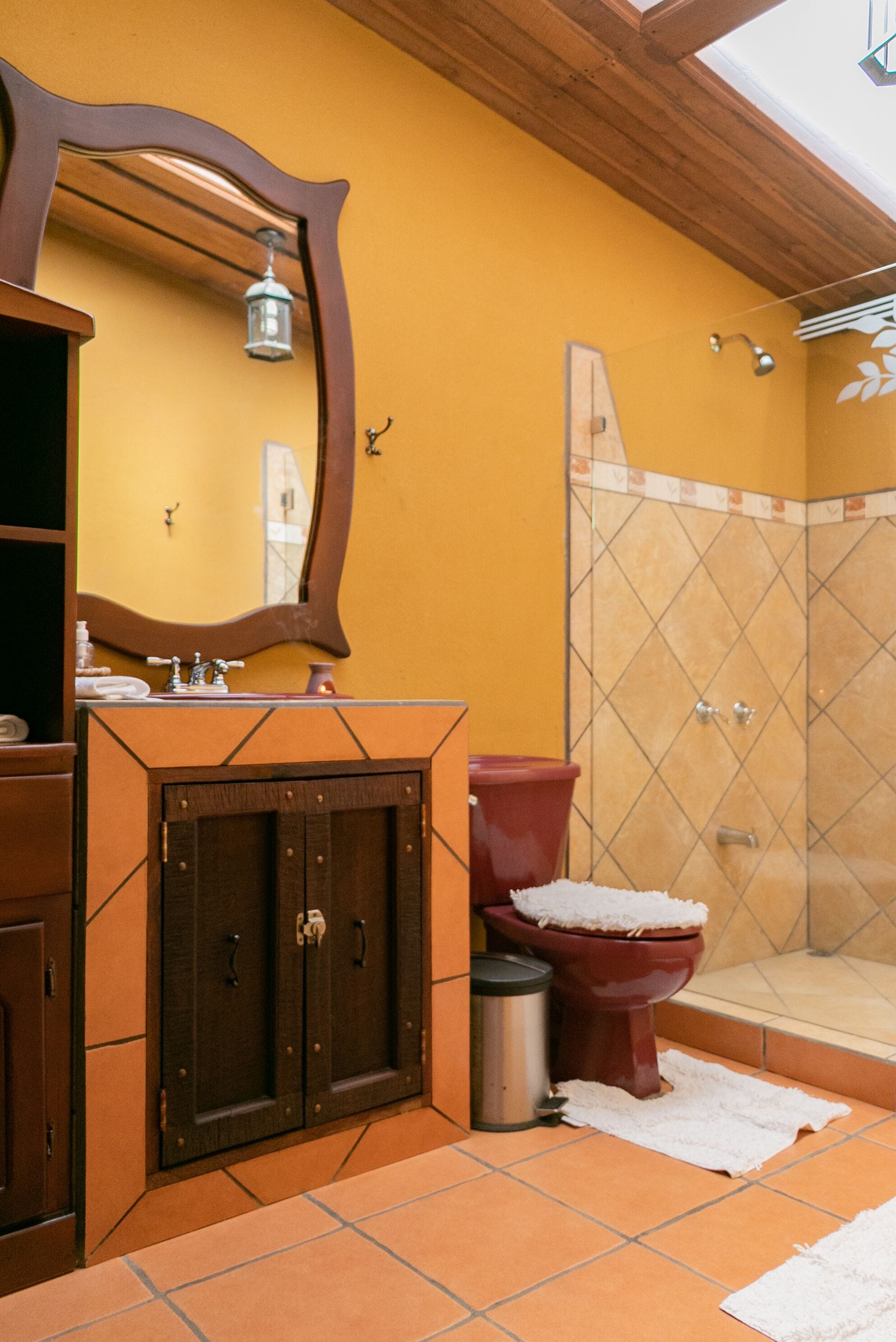A bathroom with a wooden vanity, a red toilet, a shower with a glass door, and a yellow wall.