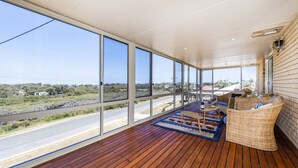 Een ruim balkon met grote ramen, rieten meubels en een houten vloer.