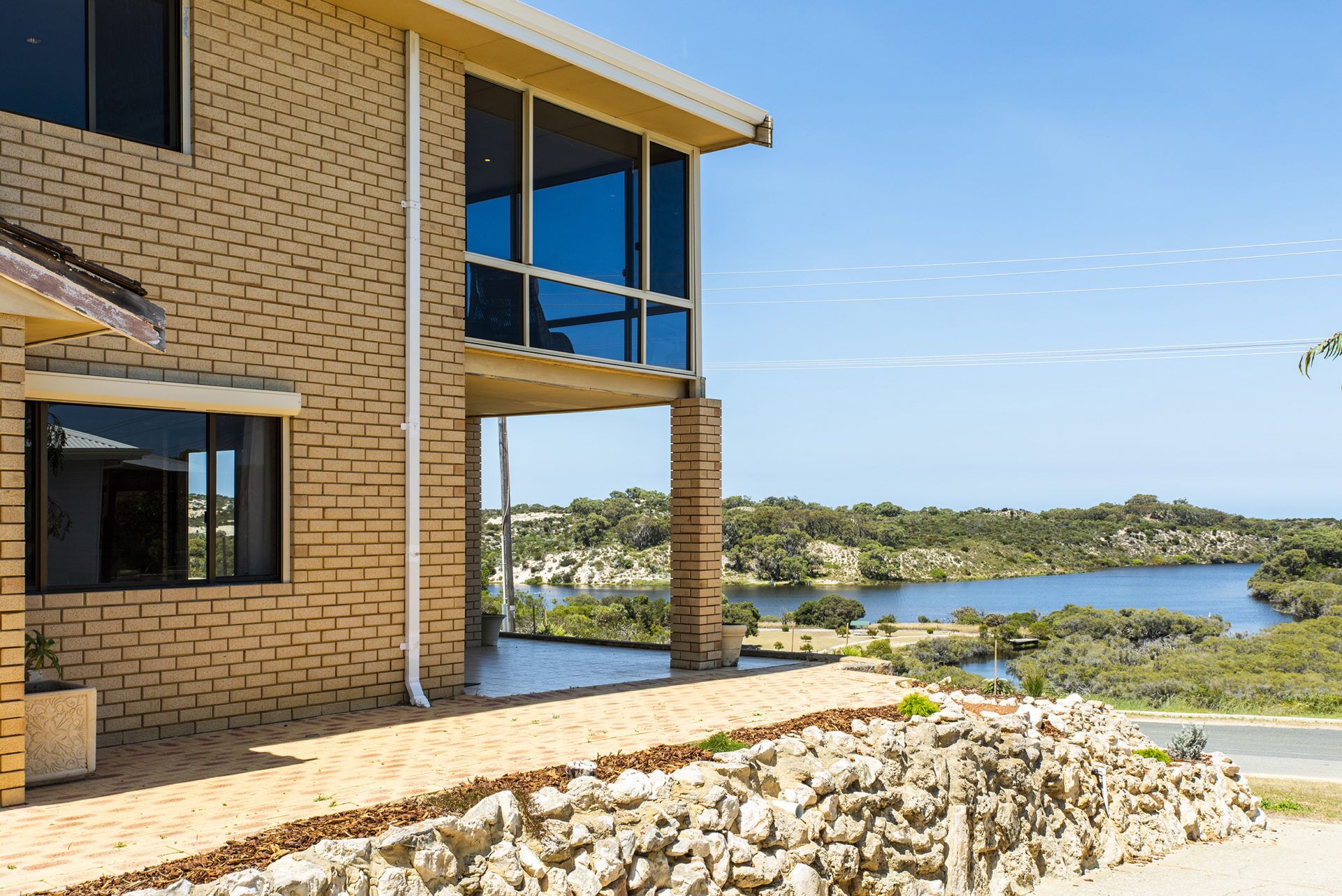 A modern two-story building with large windows overlooking a lake and hilly landscape.