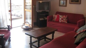 Una sala de estar con un sofá rojo, una mesa de centro de madera, un televisor y un ventanal corredero que da a un balcón.