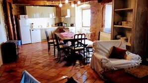 A cozy, rustic kitchen with wooden beams, a dining area with a table and chairs, and a living space with a covered sofa. - Ker Carlines (Targassonne)