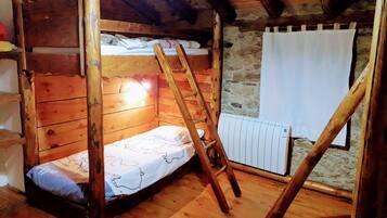 Ein Zimmer mit einem hölzernen Etagenbett, einer Leiter, einem weißen Heizkörper und einer Steinwand.