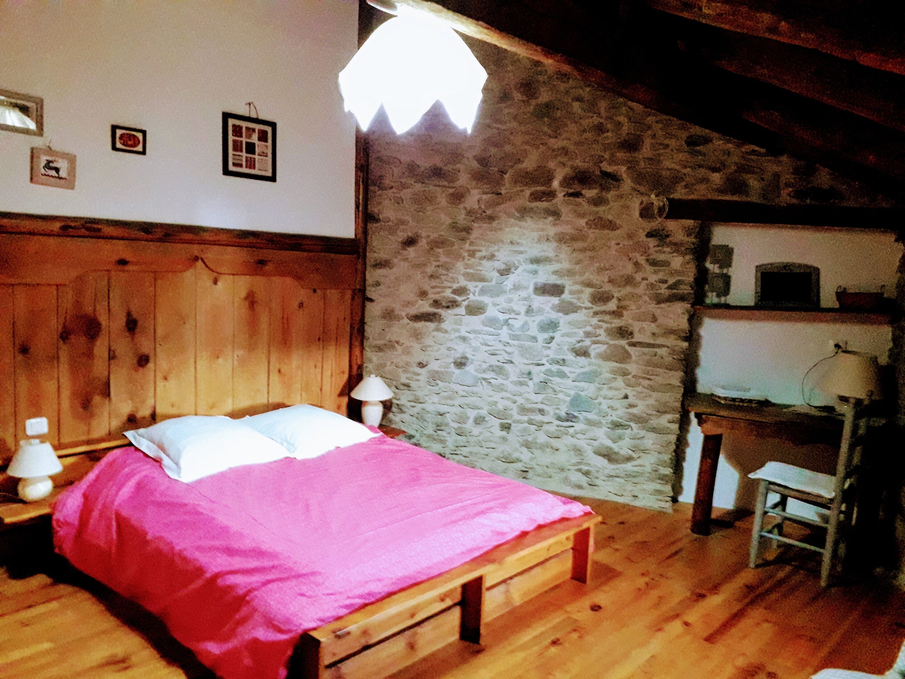 Un dormitorio con una cama de madera, una pared de piedra y un escritorio con una lámpara.