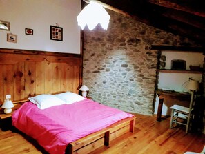 Une chambre avec un lit en bois, un mur en pierre et un bureau avec une lampe.