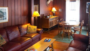 Ein gemütliches Wohnzimmer mit Ledersofas, einem Couchtisch aus Holz mit Büchern, einer Lampe und einem Hirschkopf an der Wand.