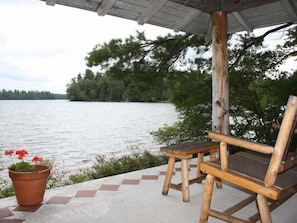 A wooden bench and a potted plant on a concrete ledge overlooking a body of water. - Gate Cottage at Pet Friendly (Paul Smiths)