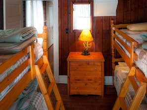 A room with bunk beds, a wooden nightstand with drawers, and a lamp with a tree design.