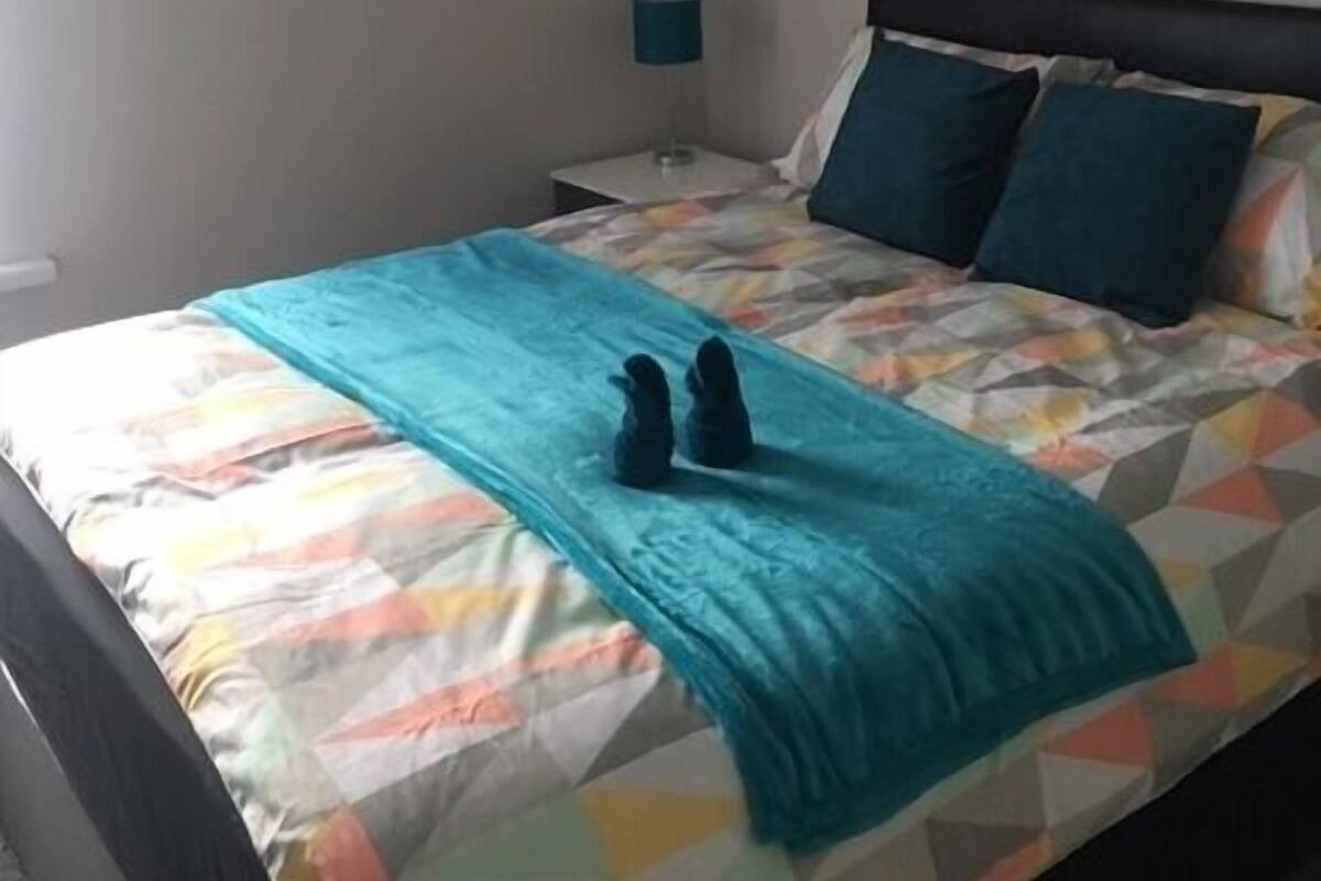 A neatly made bed with a colorful geometric-patterned bedspread and a teal throw blanket.
