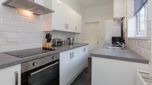 A modern kitchen with white cabinets, a built-in oven, a stainless steel range hood, and a countertop with a toaster and kettle. - Townhouse @ Corporation Street Stoke (Stoke-on-Trent)