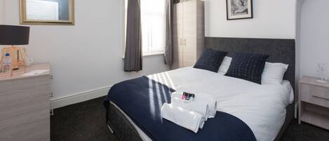 Habitación de hotel ordenada con cama, escritorio, silla y armario.