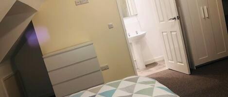 A bedroom with a bed, a white door, a bathroom with a sink, and a closet.