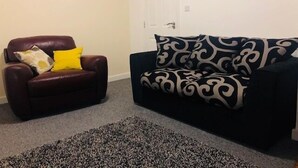 A living room with a brown leather chair, a black and white patterned sofa, a patterned rug, and a wall clock. - Townhouse @ Corporation Street Stoke (Stoke-on-Trent)