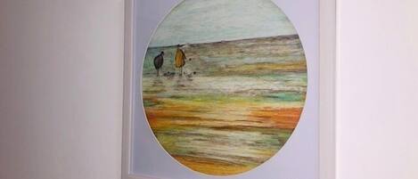 A framed painting of two figures on a beach with a signature at the bottom right.