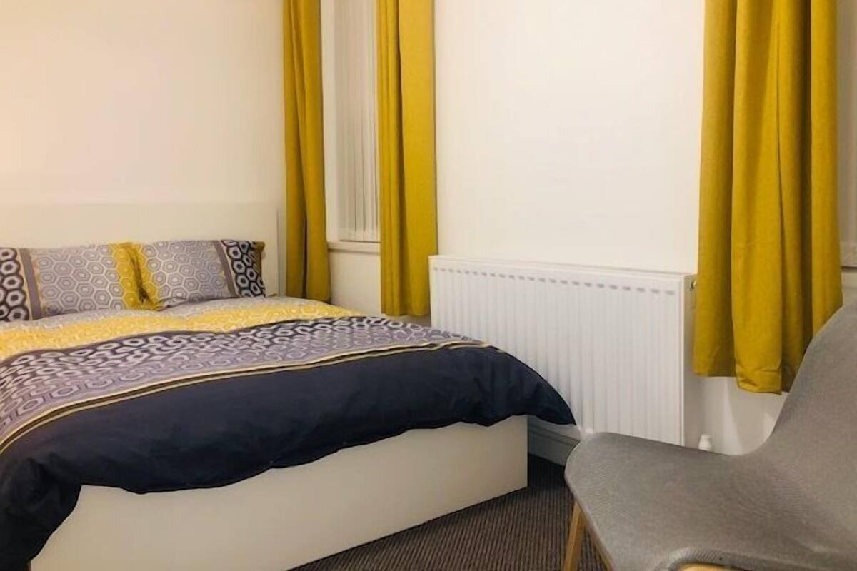 A hotel room with a bed, a chair, and a window with yellow curtains.