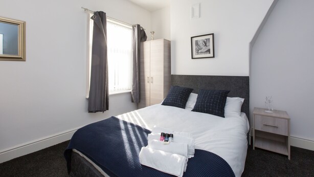 A neatly arranged bedroom with a bed, a wardrobe, a bedside table, and a framed picture on the wall. - Townhouse @ Corporation Street Stoke (Stoke-on-Trent)