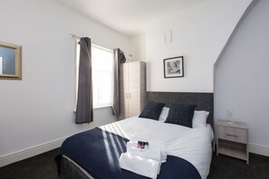 A neatly arranged bedroom with a bed, a wardrobe, a bedside table, and a framed picture on the wall. - Townhouse @ Corporation Street Stoke (Stoke-on-Trent)