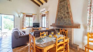 A dining area with a stone fireplace, wooden chairs, and a table set for breakfast. - Las Adelfas del Gastor by Ruralidays (Cádiz)
