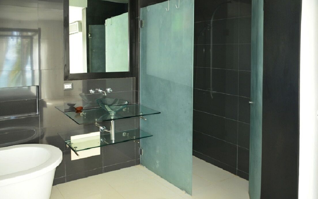 Un baño moderno con tocador de vidrio, bañera blanca y zona de ducha con azulejos oscuros.
