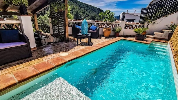 Ein rechteckiger Pool mit Fliesenrand, umgeben von Gartenmöbeln und Blumentöpfen.