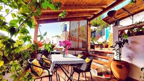Eine Terrasse im Freien mit Tisch und Stühlen, umgeben von Kübelpflanzen und einer Holzpergola.