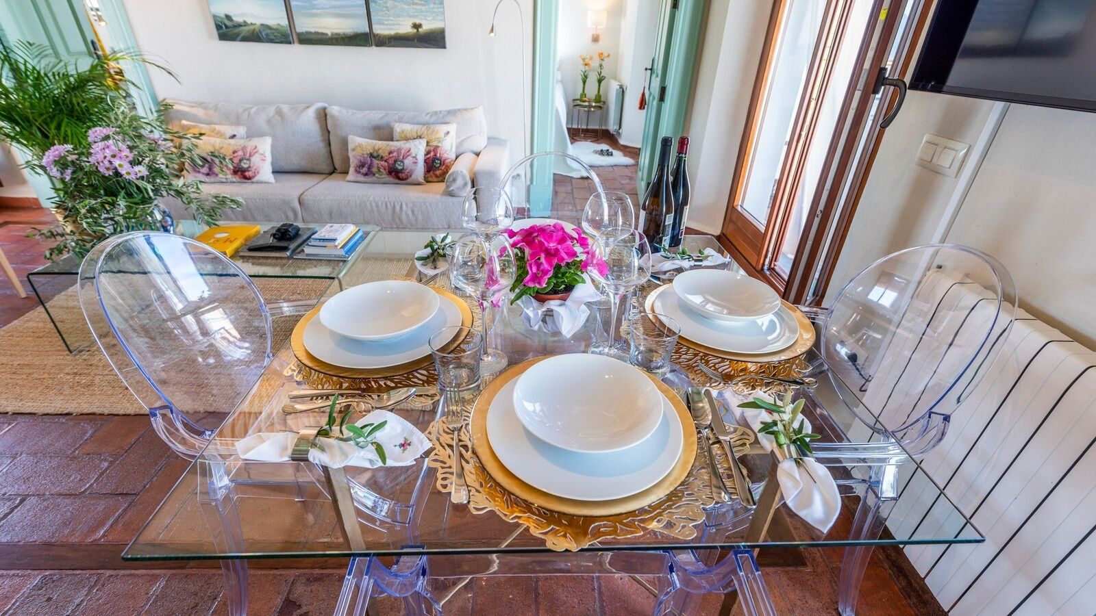 A dining table set with clear glassware, gold-rimmed plates, and a vase with pink flowers.