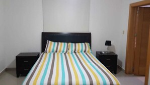 Un dormitorio con cama, dos mesitas de noche, una lámpara y una puerta de madera.