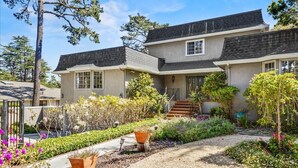 Een tweelaags huis met een veranda, een trap en een goed onderhouden tuin met diverse planten en bloemen.
