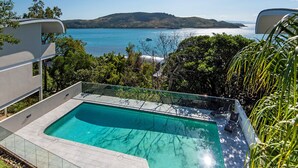 Una piscina infinita moderna con vistas despejadas al mar y colinas lejanas.