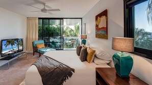 Un dormitorio moderno con una cama grande, televisión, balcón y vistas a palmeras, además de un ventilador de techo.