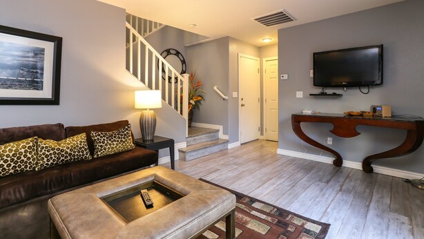 Un salon avec un canapé en cuir marron, une table basse, un téléviseur fixé au mur, un escalier et une porte donnant sur une autre pièce.