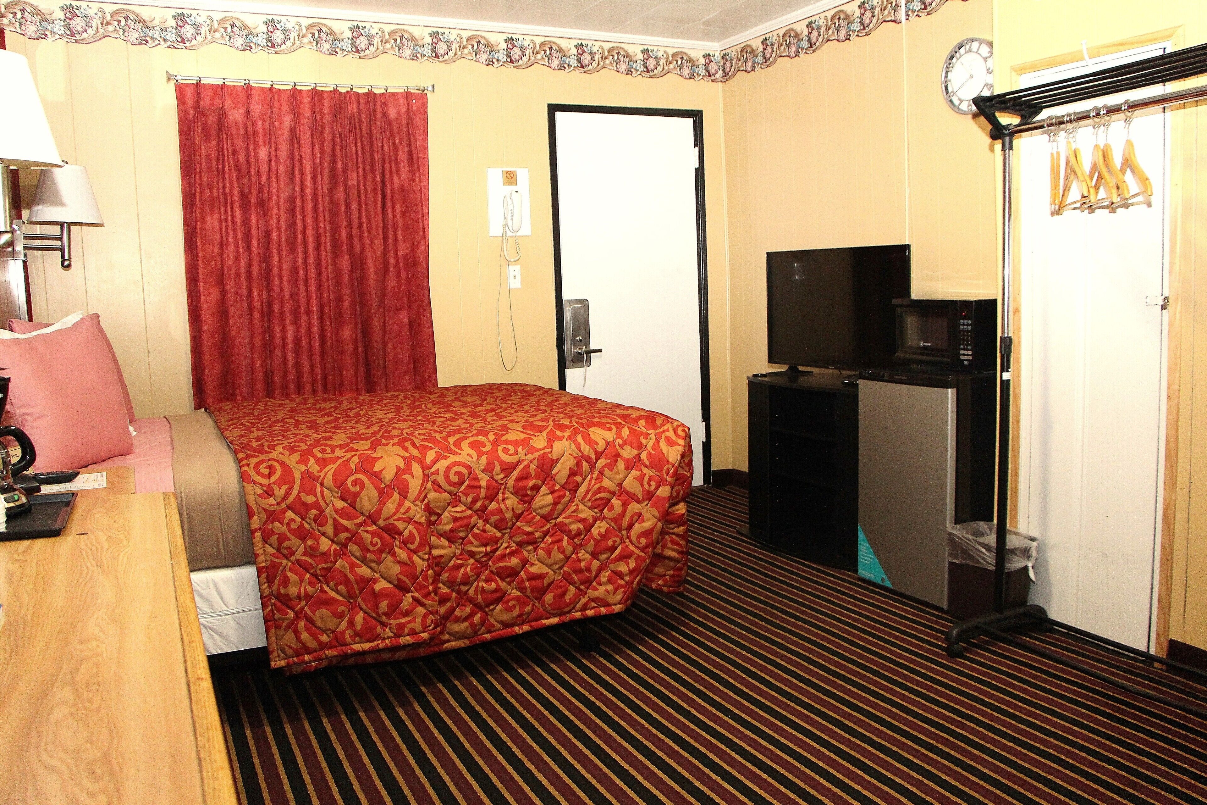 A hotel room with a bed, a desk, a television, a microwave, and a wardrobe.