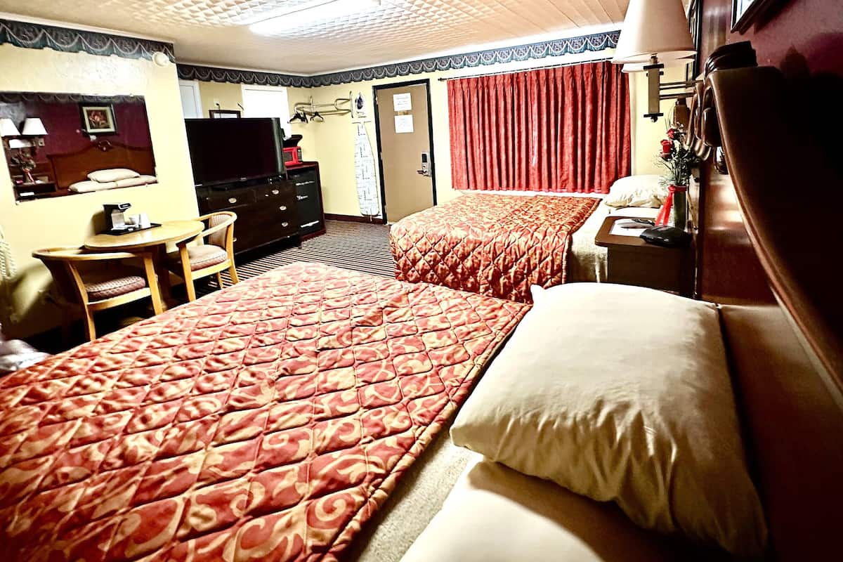 Une chambre d’hôtel avec deux lits, un bureau, une chaise, une télévision et une commode.