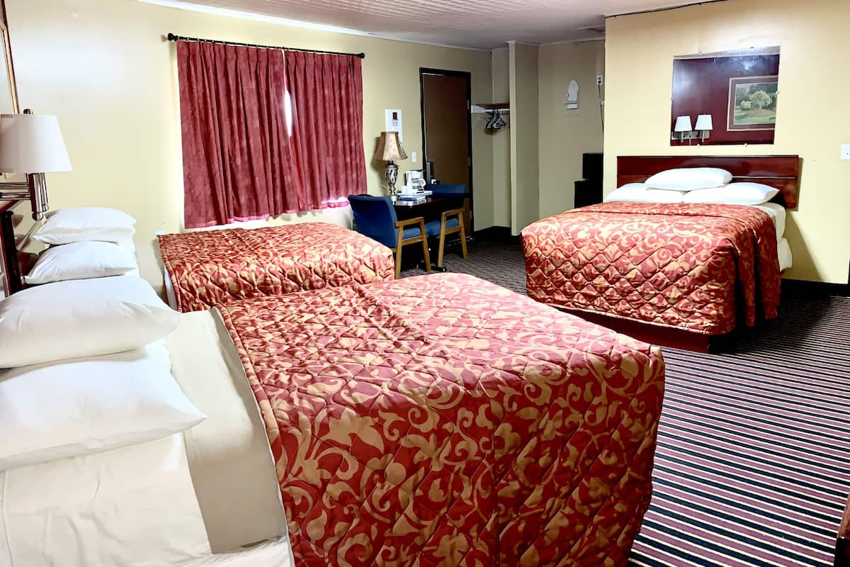 Une chambre d’hôtel avec deux lits, un bureau, une chaise, une lampe et une fenêtre avec des rideaux.