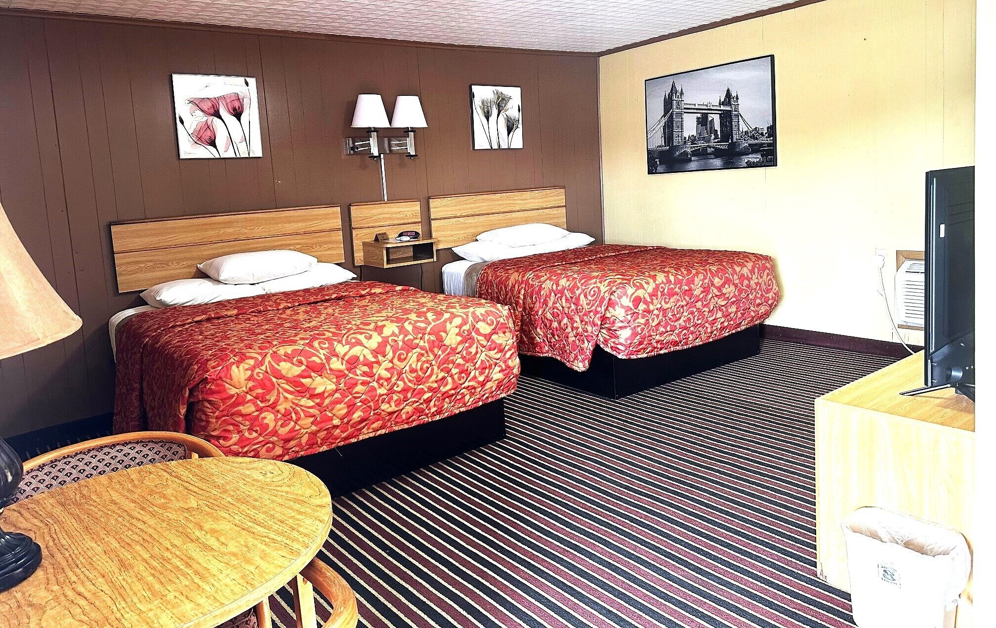 A hotel room with two beds, a desk, a chair, a TV, and artwork on the walls.
