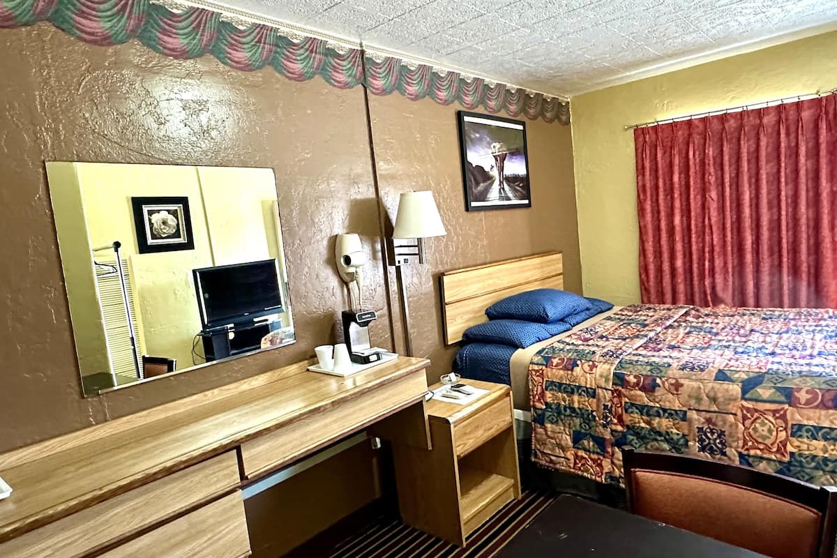 Une chambre d’hôtel avec un lit, un bureau avec une lampe, un téléphone et un miroir.