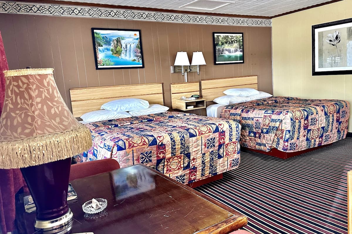 Une chambre d’hôtel avec deux lits, une table de chevet, une lampe et deux tableaux encadrés au mur.