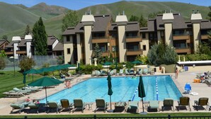 A hotel with a swimming pool, outdoor seating, and a mountainous backdrop.