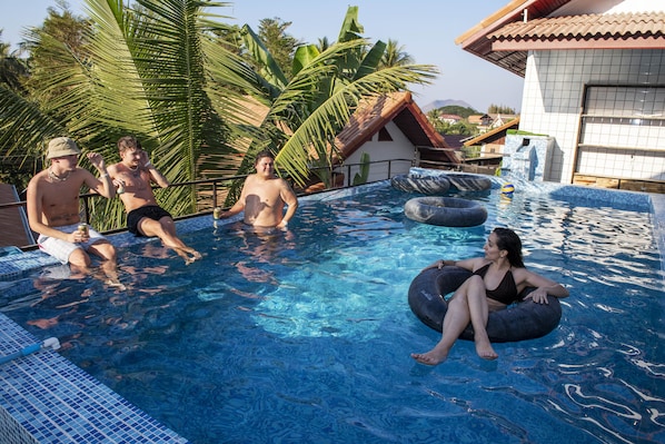 Una piscina con agua azul cristalina, rodeada de palmeras y un edificio con techo de tejas.