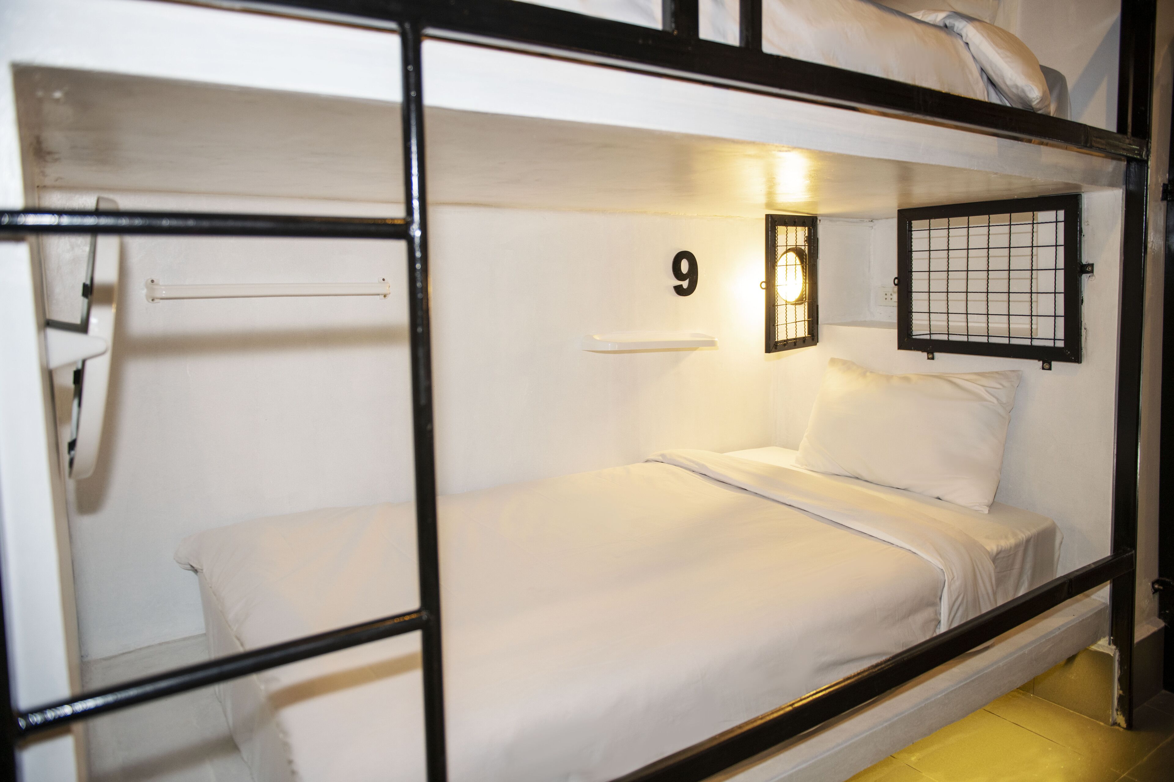 A bunk bed with a number '9' on the wall, a small window with a grid pattern, and a light fixture above the window.