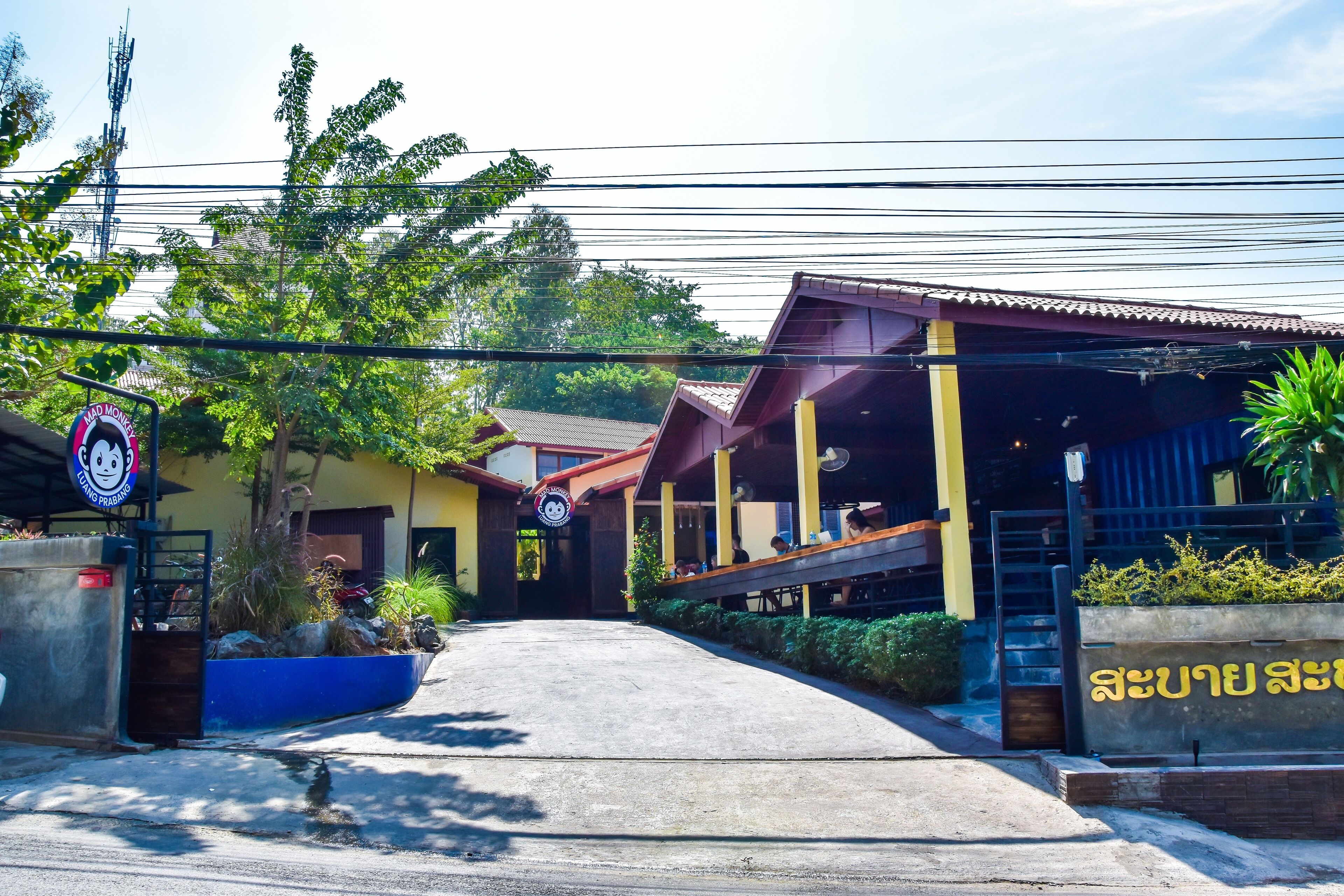 A building with a covered entrance, outdoor seating area, and a sign with Thai script.