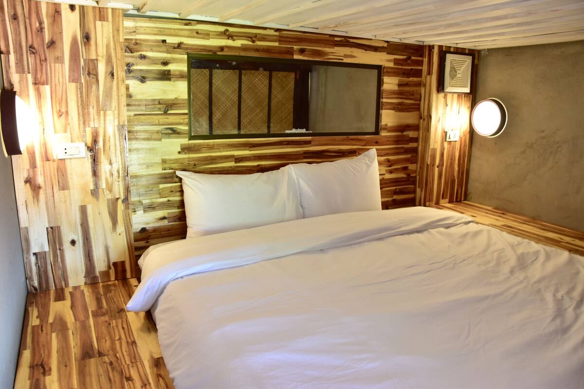Ein Schlafzimmer mit Holzwandverkleidung, einem Bett, einem Fenster und einer Wandleuchte.