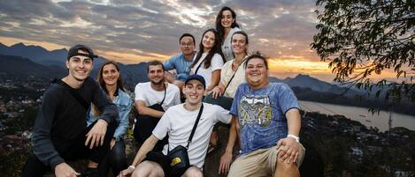 A group of people sitting on a rock with a scenic view of mountains and a river in the background.