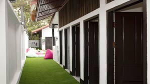 A narrow corridor with artificial green turf, a row of dark wooden doors, and a pink inflatable play structure in the background. - Mad Monkey Luang Prabang (Luang Prabang)