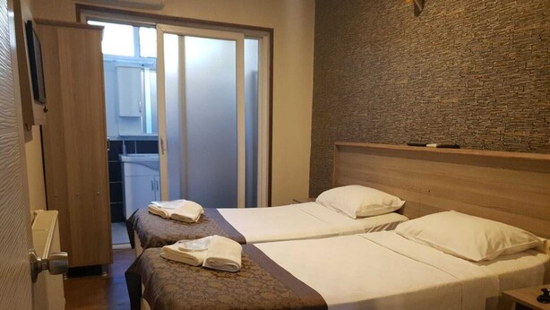 Une chambre d’hôtel avec deux lits, une tête de lit en bois, un mur en pierre et une salle de bain visible à travers une porte coulissante.