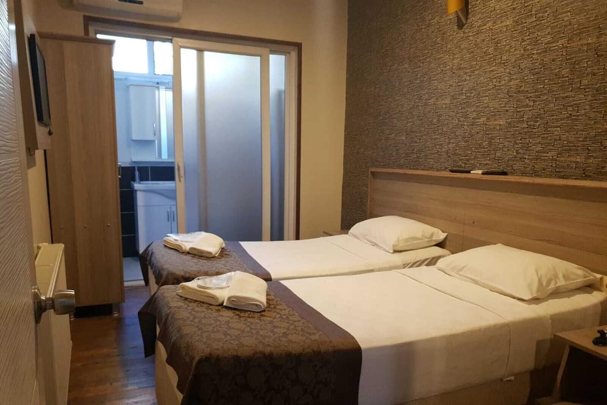 A hotel room with two beds, a wooden headboard, a stone wall, and a bathroom visible through a sliding door.