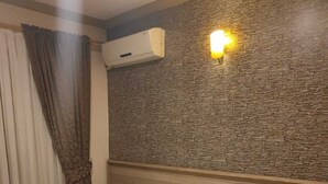 Une chambre d’hôtel comprenant un lit, une table de chevet, un climatiseur fixé au mur et un luminaire décoratif.