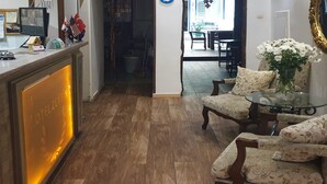 Un espace d’accueil avec un comptoir en bois, un écran d’ordinateur et un tableau d’affichage. On aperçoit à l’arrière-plan un coin repas avec une table et des chaises.